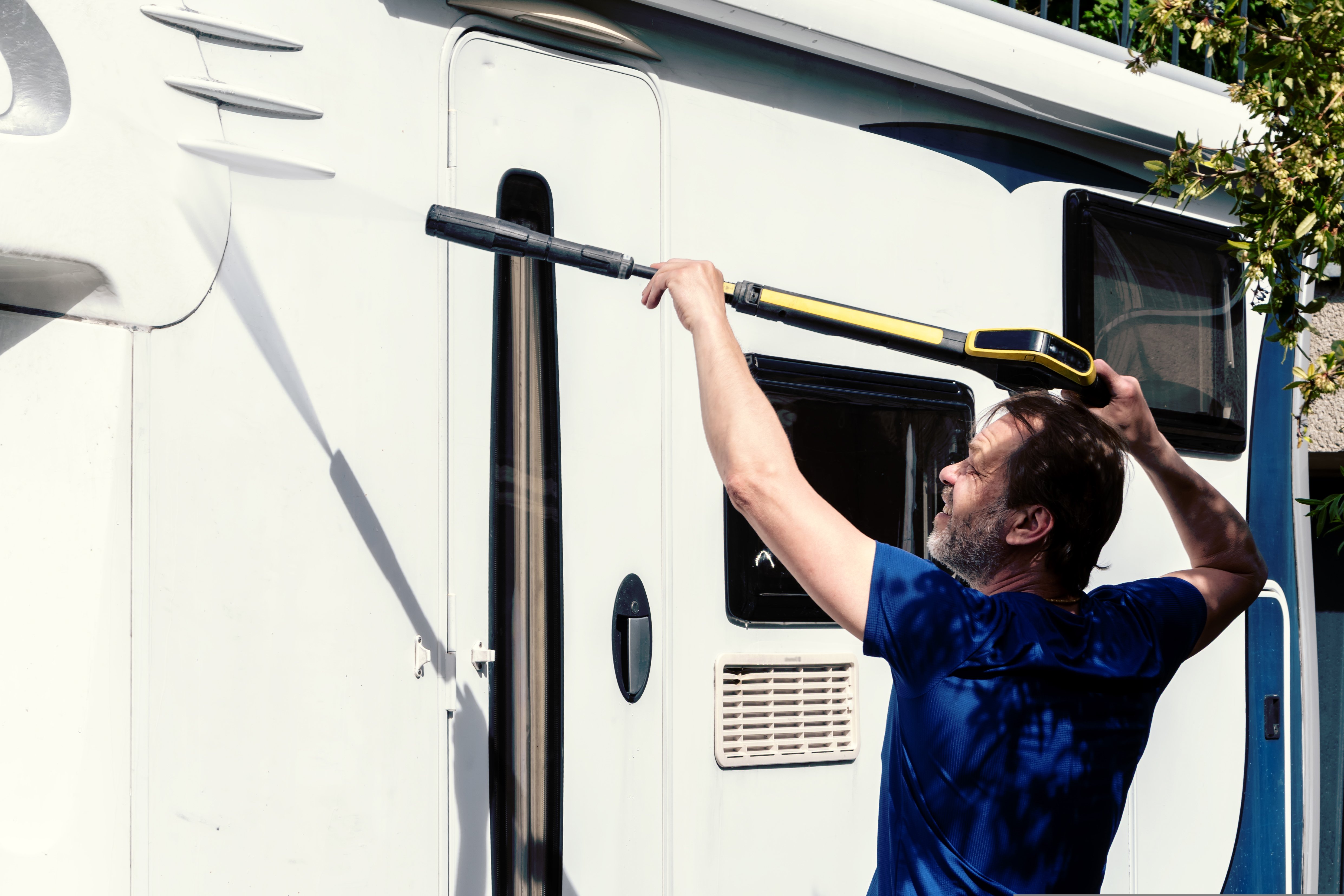 Camper owner washing exterior body of motorhome during seasonal maintenance cleaning